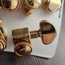 Zlaté ladicí mechanismy na bílém podkladu. Na jednom z nich je vyryt nápis GROVER. V pravém horním rohu je vidět část textu 25 USA WWW.GROTRO.COM. Po…