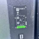Detail zadní strany černého reproduktorového boxu s připojeným panelem konektorů. Na panelu jsou nápisy LD SYSTEMS STINGER 15, powered by BMS a logo…