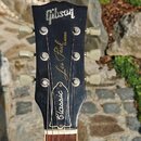 Černá hlava elektrické kytary s bílým logem Gibson. Na hřidnu je nápis Les Paul CLASSIC a v dolní části nápis Classic. Kytara má šest bílých ladiček…