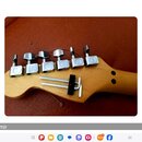 Fotografie zachycuje hlavu kytary z přírodního dřeva s instalovanými kovovými ladicími mechanismy stříbrné barvy. Na hlavě je rovněž umístěn kovový p…