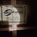 Fotografie zachycuje vnitřní štítek kytary přilepený na dřevěnou desku. Na štítku je černé logo soundsation guitars a nápis Model BCE-500M. Dole je u…