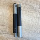 Dvě kovové válcové součásti mikrofonu v kombinaci stříbrného a černého povrchu. Na horní části levé součásti je nápis M 7, na spodní části je viditel…