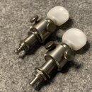 Dvě ladicí mechaniky z kovu s bílými plastovými knoflíky ve tvaru kuliček. Povrch kovových částí vykazuje známky opotřebení a oxidace. Na mechanikách…