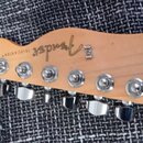 Detail hlavy kytary z přírodního dřeva. Na povrchu je nápis TELECASTER® a logo Fender. Jsou zde vidět šest chromovaných ladiček.