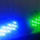 Dvě LED osvětlovací panely v zapnutém stavu. Levý panel svítí modře a pravý zeleně, oba mají mřížku malých světelných bodů. Na zařízeních nejsou vidi…