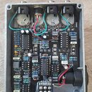 Interiér hliníkového šasi s elektronickým plošníkem efektového pedálu. Na černé desce jsou osazeny integrované obvody, kondenzátory a potenciometry s…