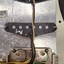 Fotografie zachycuje vnitřek kytary s dvěma snímači typu single-coil a kovovou elektronickou schránkou. Snímače mají černé plasty, na kterých jsou vi…