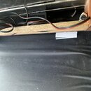 Detailní pohled na vnitřek šasi nebo skříně s viditelným zapojením černých kabelů. Součástí je dřevěná deska z OSB a v pozadí jsou vidět elektronické…