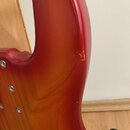 Detail korpusu elektrické kytary s červeným gradientem (sunburst). Povrch je lakovaný a v pravé části jsou viditelné škrábance a oděrky laku. Na fotc…