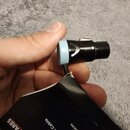 Ruka drží černý kabel s modrým plastovým prstencem u konektoru. Na černé části konektoru je bílý nápis STUDIOSPARES. Kabel je částečně v černém papír…