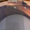 Detailní pohled na pružiny snare drumu (čochrlíky) v kovovém rámu. Na horním rámu je vyryt nápis PURESOUND™. Nástroj má dřevěný korpus a na bláně je…