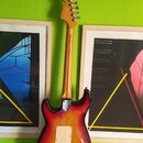 Zadní strana elektrické kytary s tělem v červeno-žlutém sunburst provedení a javorovým hřidlem. Na kovovédesce u základny krku je viditelný nápis, kt…