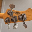 Zadní strana hlavy basové kytary z přírodního dřeva. Jsou na ní vidět čtyři chromované ladičky a nápis MADE IN SAN LUIS OBISPO CALIFORNIA, USA. Na ho…