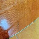 Detailní záběr na lakovaný dřevěný povrch hudebního nástroje v hnědavé barvě s viditelnou sletovkou dřeva. V dolní části je patrná svislá škrábance n…