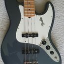 Šedá elektrická basová kytara s bílým pickguardem a hnědým hmatníkem. Na bílém pickguardu je čitelné logo Fender. Nástroj má dva snímače a tři ovláda…