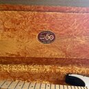 Interiér kufrů s oranžovou plyšovou výplní. Uprostřed je oválná nálepka s nápisy STRATOCASTER™, Fender 50 ANNIVERSARY 1954–2004. Ve spodní části je v…