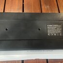 Spodní strana černého elektronického zařízení s gumovými nožičkami. Na bílém štítku je uveden nápis DONNER Sym Bass Analog Synthesizer and Sequencer,…