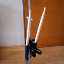 Na kovovém stojanu pod činelem je upevněn černý držák na paličky. V držáku jsou umístěny dvě dřevěné bubnové paličky světlé barvy. Na fotce nejsou žá…