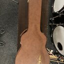 Hnědý kufr na kytaru v podobě akustického nástroje. Na spodní části je zlatý nápis „Epiphone“ a „Gibson“. Povrch kufrů vykazuje drobné známky opotřeb…