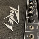 Detailní záběr na černý kytarový zesilovač s texturovaným povrchem. Na čelní straně je stříbrné logo "Randall". Ovbedací panel obsahuje knoflíky s ná…