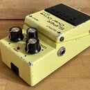 Žlutý kytarový efekt s černým spínacím pedálem. Na horní části je nápis BOSS SUPER OverDrive SD-1 a označení vstupů INPUT a OUTPUT. Na boku jsou tři…