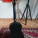 Černá akustická kytara z pohledu zezadu. Nástroj je v matném provedení, na hlavě jsou vidět šest ladicích mechanismů s bílými knoflíky. Povrch kytary…