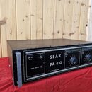Černý výkonový zesilovač v kovovém šasi s úchopy po stranách. Na předním panelu je bílý nápis SEAK PA 410 a POWER AMPLIFIER, dále přepínače LOW PASS…
