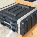 Černý transportní kufr z texturovaného plastu s hliníkovými hranami a kovovými zámky. Na boční straně je vidět nápis "flightcase". Povrch vykazuje mí…