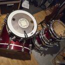 Sada červených bubnů s kovovým hardwarem. Na bílém blaně největšího bubnu je vidět nápis EVANS a logo s textem EQ3. Na menším bubnu je vidět nápis EV…