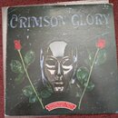 Fotografie zobrazuje obal vinylové desky s nápisem CRIMSON GLORY v horní části. Uprostřed je zobrazen kovový maskovaný obličej obklopený dvěma červen…