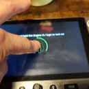 Detailní záběr na displej DJského kontroléru s nápisem „hold the Engine DJ logo to turn on“. Na obrazovce je vidět zelený obrys loga, na které dopadá…
