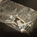 Průhledný plastový sáček, uvnitř kterého se nachází kovové příslušenství stříbrné barvy. Na sáčku je vidět recyklační symbol a nápis LOPE. V levém ho…