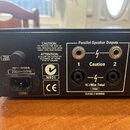 Zadní strana černého elektronického zařízení s několika konektory. Jsou zde dva páry výstupů označené jako Parallel Speaker Outputs (čísla 1 a 2) s v…