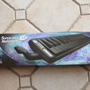 Kartonová krabice s černou melodikou. Na obalu jsou nápisy SUPERFORCE 37 Melodica, HOHNER a slogany For unlimited Creativity a From the original inve…