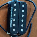 Černý humbucker s dvěma cívkami a viditelnými polkovými magnety. Na jedné z cívek je bílý nápis Seymour Duncan. Snímač má připojený černý kabel a je…