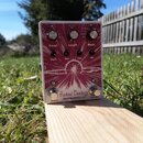 Kytarový efekt v červeném provedení s bílým grafickým motivem paprsčitých čar. Na spodní části je nápis Astral Destiny a pod ním značka EarthQuakerDe…