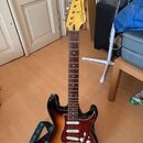 Elektrická kytara s tělem v provedení sunburst a žlutou hlavou. Na hlavě je vidět nápis "Stratocaster" a "MADE IN MEXICO". Kytara má hnědý hmatník, b…
