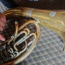 Detailní záběr na mosazný dechový nástroj, pravděpodobně tubu nebo souslovný instrument. Na povrchu je vidět kulaté logo s nápisem "G. COURTOIS PARIS…