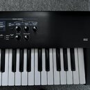 Černý digitální klavír s bílými a černými klávesami. Horní panel nese nápis PATCH MODIFY a obsahuje ovládací prvky jako CUTOFF, RESONANCE a přepínače…