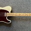 Krémová elektrická kytara s tmavě červeným pickguardem a světlým hnedým hmatníkem. Na hlavě kytary je viditelné logo Fender a nápis MADE IN MEXICO. N…