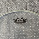Průhledná bubenová blána s černým potiskem. Uprostřed je logo koruny a nápisy REMO®, AMBASSADOR® CLEAR, MADE IN U.S.A. Povrch je hladký a bez viditel…