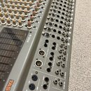 Šedý mixovací pult s velkým množstvím potenciometrů a posuvníků. Na boku je viditelný nápis M-2524 a logo TASCAM. V pravé části jsou různé konektory…