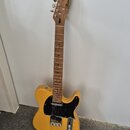 Elektrická kytara s přírodním žlutým povrchem těla a hnědým hmatníkem. Na hlavě je viditelné logo "Brand". Kytara má černý pickguard a kovový most sá…