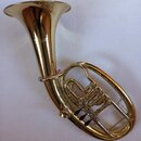 Zlatavý mosazný horn s nápisem "The Conn" a pod ním menším slovem "ELKHART". Nástroj je v lesklém stavu bez viditelných škrábanců či opotřebení. Na f…