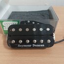Černý humbucker s dvěma řadami magnetických pólů. Na spodní části je bílý nápis Seymour Duncan. Povrch plastového krytu vykazuje drobné škrábance a z…