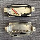Dvě kytarové snímače s kovovým krytem v bílé a stříbrné barvě. Horní snímač má nápis Seymour Duncan, Made in America a na boku štítek s textem SH1N N…