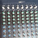 Detailní pohled na míchací pult značky YAMAHA. Jsou vidět řady ovládacích prvků s nápisy jako GAIN, HIGH, MID, LOW a AUX. Knoflíky jsou provedeny v b…