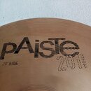 Detail kovového činely v bronzové barvě s viditelným koncentrickým rýhováním. Na povrchu je černý nápis Paiste a pod ním označení 20" RIDE. Vedle je…