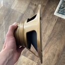 Fotografie zachycuje reproduktor v profile, který drží ruka. Reproduktor má zlatavý kovový rám a tmavou membránu. Na povrchu nejsou viditelné žádné z…