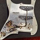 Fotografie zachycuje rubickou stranu bílého pickguardu k elektrické kytáře s instalovanou elektronikou. Jsou zde vidět dva humbuckery, potenciometry…